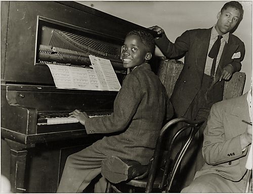 Ahmad Jamal seated on instrument case playing the piano