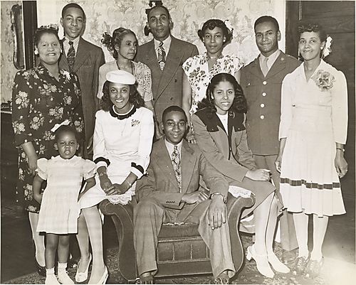 Three generations of a family grouped around armchair in domestic interior