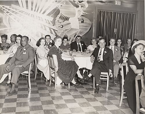 Men and women at tables in club? with mural of musical instruments