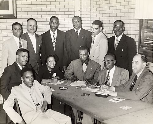 Eleven men, possibly including Mr. Hill seated second from right, William Harris, Carl Redwood, Mr. Boyd, and one woman, around a meeting table