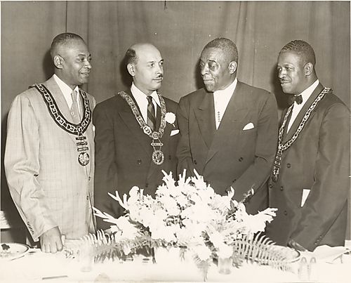 Four men, including Judge Homer S. Brown and his law partner Richard Jones, Louis J. McTurner, and Carl Brown standing behind flower arrangement, at an Elks dinner