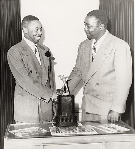 Two men shaking hands behind football trophy