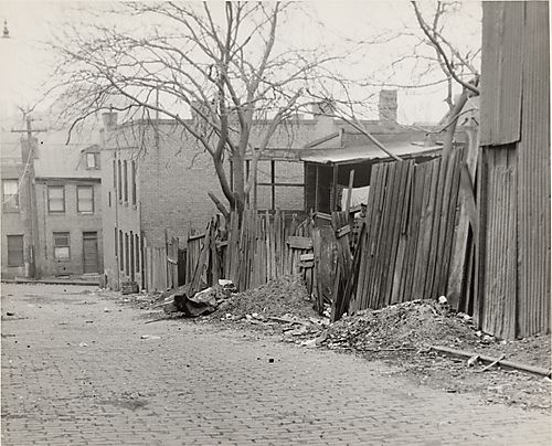 Brick road off Wylie Avenue with trash and dilapidated wood fence to right