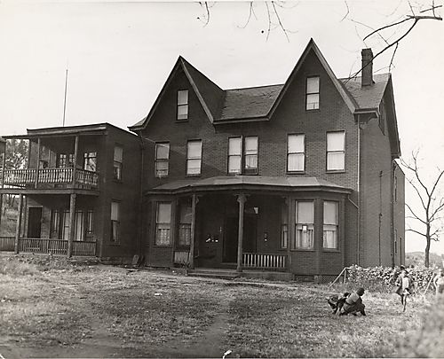 Large brick house with four children playing in yard