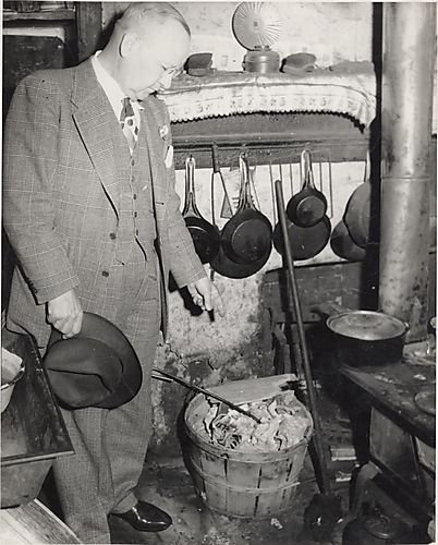 Detective in old fashioned kitchen pointing to basket of rags and paper
