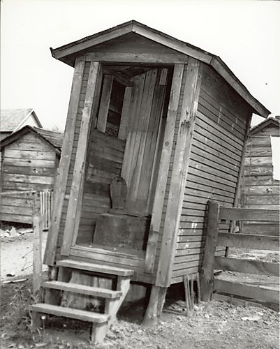 Leaning outhouse surrounded by other wooden structures