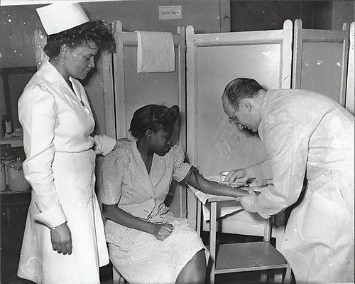 Doctor drawing blood from a woman, with nurse, Mrs. Eunice Cook, in attendance