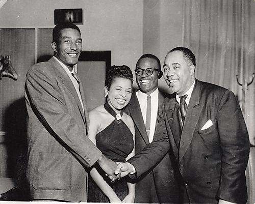 Two men shaking hands, with a woman and Bill Powell, WAMO disc jockey, in center