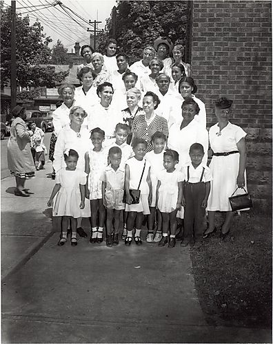 Women posed on steps with children in front, possibly a church group, political sign? for Garrett in background