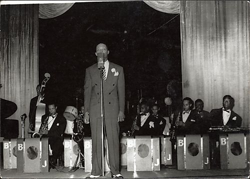 Man at microphone with jazz group, possibly the Bobby Jones Band, in background