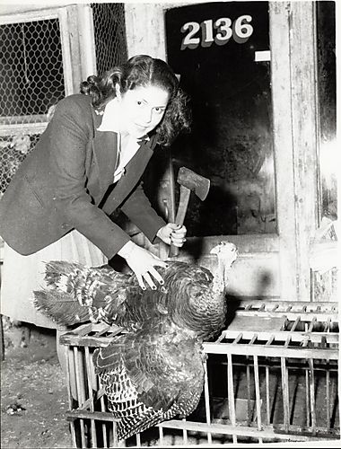 Mrs. Wyonella Croft with ax and turkey in front of a market, street no. 2136