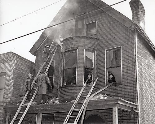 Fire fighters with ladders and hoses on second and third floors of brick house