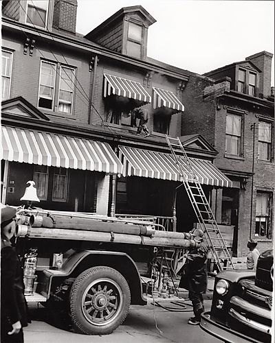 Fire fighter on porch roof of a row house with fire truck parked below
