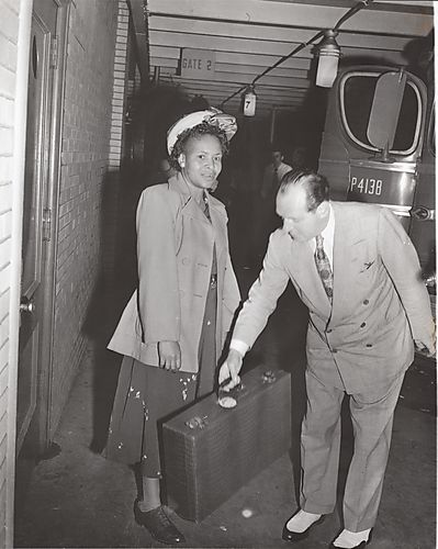 Man assisting woman holding crocodile suitcase next to a Greyhound bus