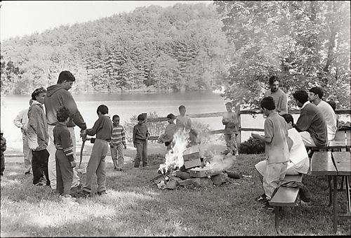 Men and boys at a campfire by a lake