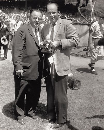 Joe Garagiola with camera and another man at Forbes Field, with Chicago Cubs baseball player in background