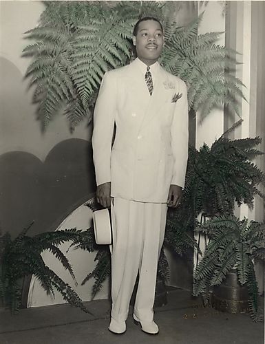 Fashion model Louie Smith in white suit standing and holding hat