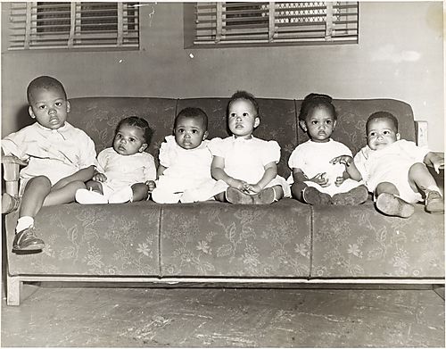 Six small children and babies lined up on sofa