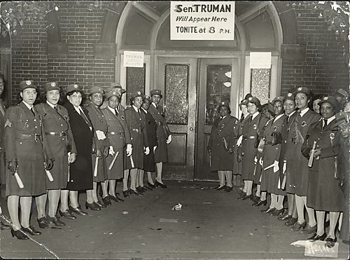 Uniformed women gathered in formation in front of building entrance with sign reading: Sen. Truman Will Appear Here Tonite at 8 p.m.""