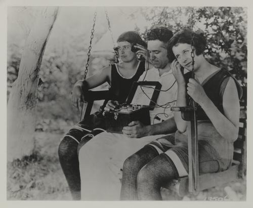 Three people on a swing listening to a radio