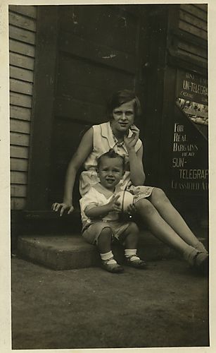 A young woman and Dickie Fuchs, as a toddler, seated in front of the Frick Park Confectionary
